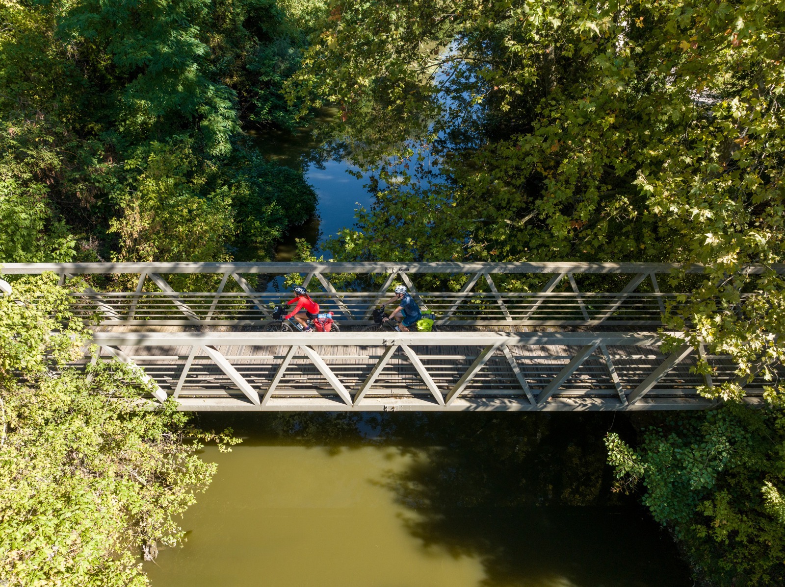 Deux personnes à vélo en train de passer sur une petite passerelle entourée de végétation et d'eau